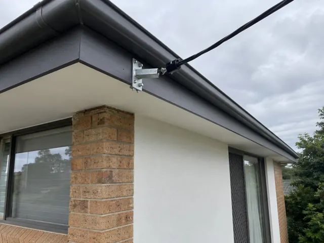 Overhead service cable and point-of-attachment bracket on a brick house under the eaves in Budgewoi